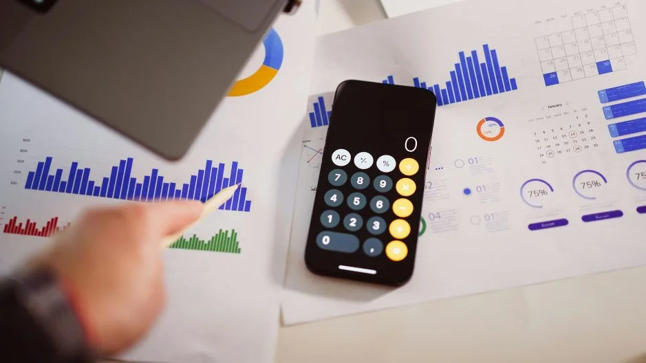 Photo of charts, calculator, and phone representing AI budget overruns and unrealistic expectations