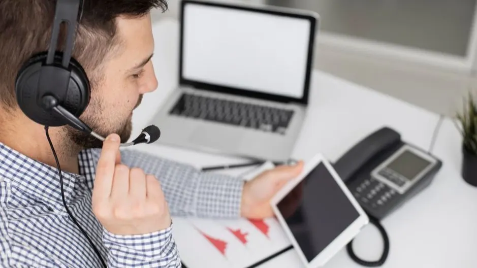 Customer support agent with headset reviewing a tablet at a workstation with a laptop and office phone