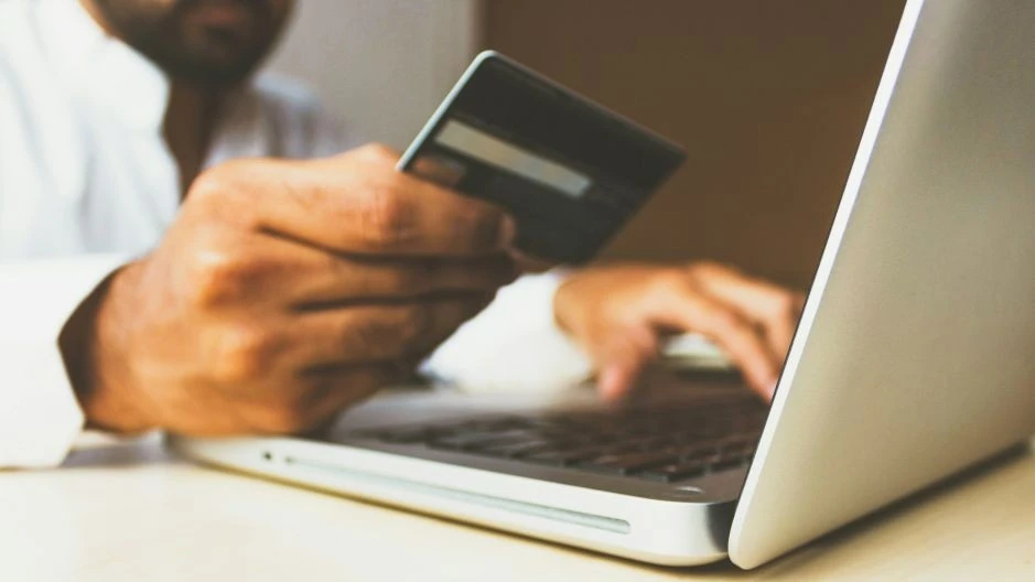 Close-up of a person in a white shirt holding a credit card, for order payment on a laptop